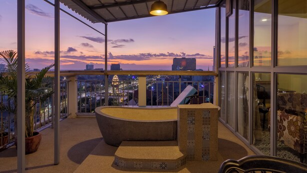 A balcony with a curved seating area, large windows, and a cityscape view at dusk. - ARISON Hotel (Phnom Penh)