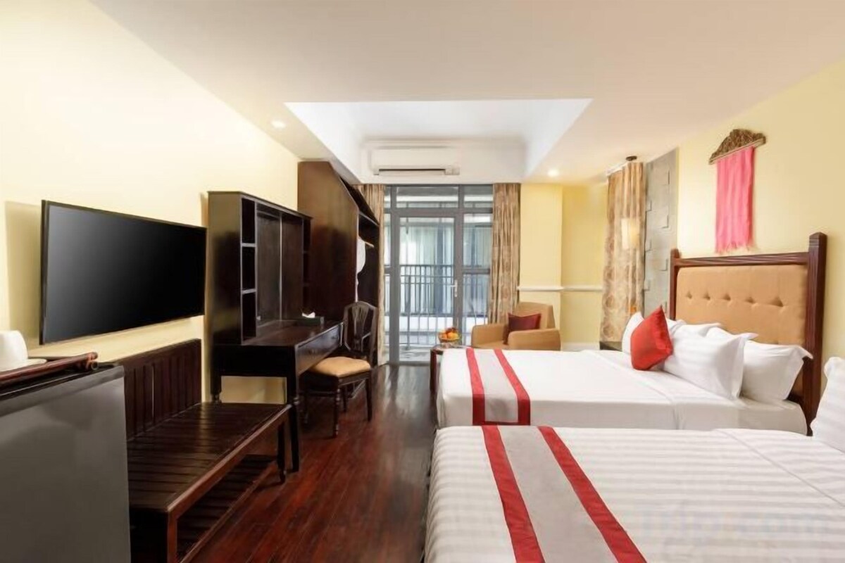 A hotel room with a TV, a desk, two beds, and a view of the outdoors.