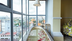 A bathroom with a bathtub filled with water and rose petals, large windows offering a city view, and a hanging light fixture. - ARISON Hotel (Phnom Penh)