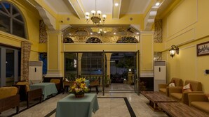 A hotel lobby with a marble floor, yellow walls, and a chandelier. There are tables with chairs and a reception desk. - ARISON Hotel (Phnom Penh)