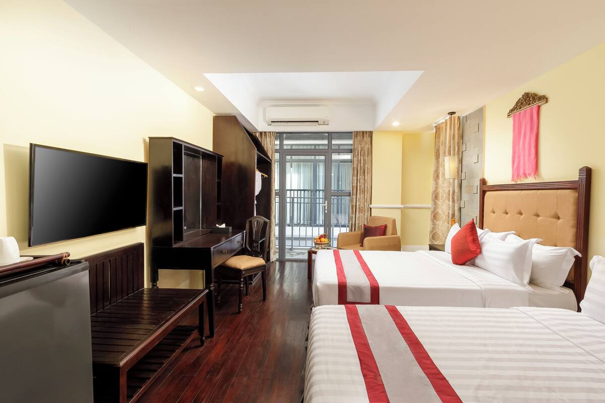 A hotel room with two beds, a TV, a desk, and a view of the outside.