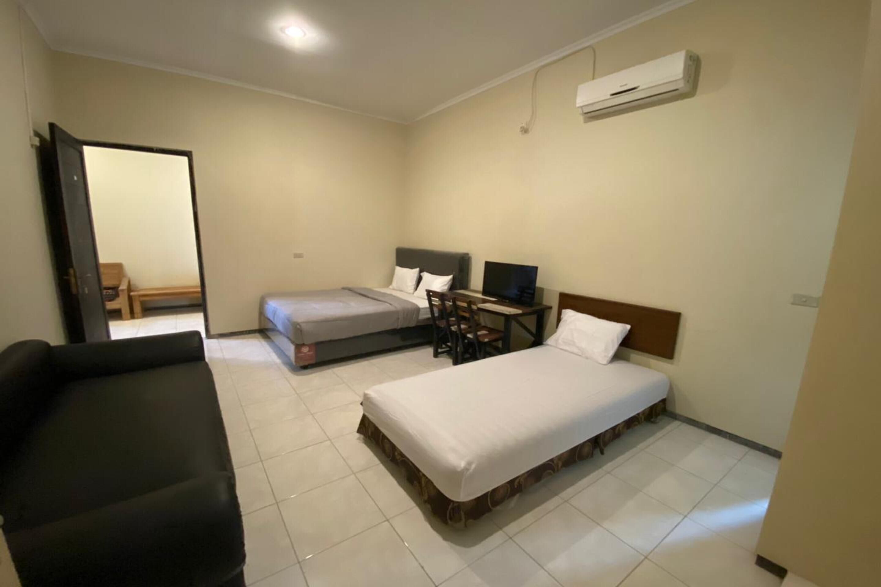 Habitación de hotel con dos camas, un escritorio, una silla, un sofá y un equipo de aire acondicionado.