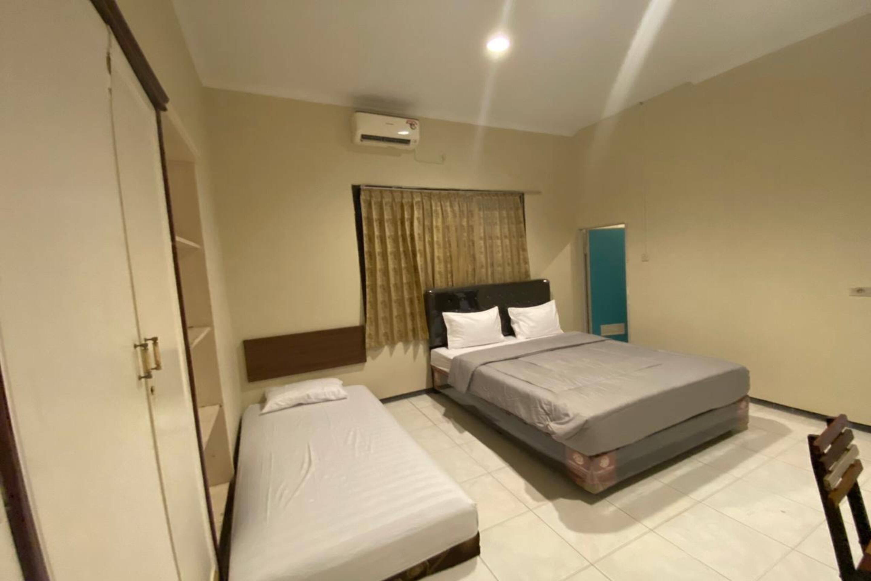 Quarto de hotel com duas camas, um guarda-roupa, aparelho de ar condicionado e cortina.