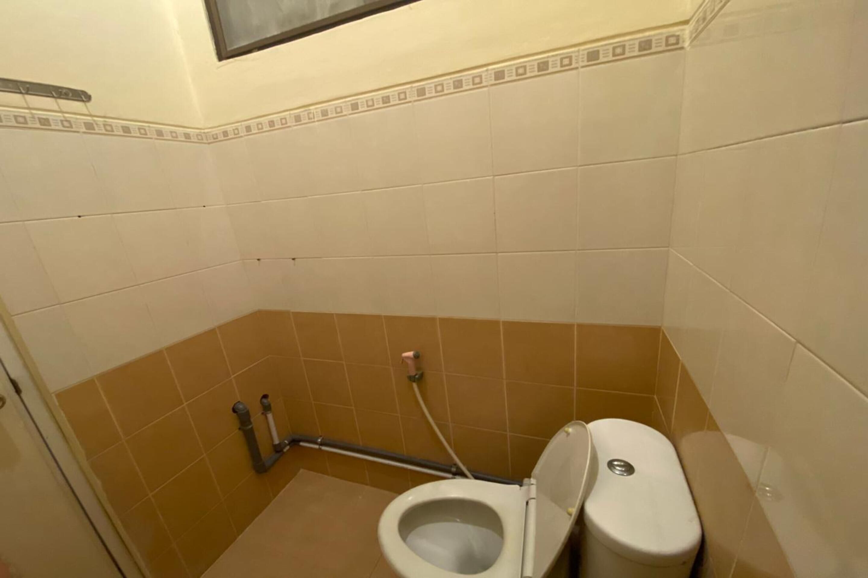 A small, compact bathroom with a toilet, a handrail, and a wall-mounted faucet.