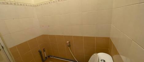 A small, compact bathroom with a toilet, a handrail, and a wall-mounted faucet.