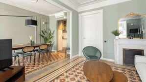 A modern living room with a dining area, a fireplace, and a large mirror. - Spacious Stylish 4-BR Modernist Apartment (Barcelona)