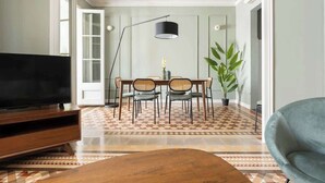 A living room with a television, dining table, chairs, a lamp, and a plant. - Spacious Stylish 4-BR Modernist Apartment (Barcelona)