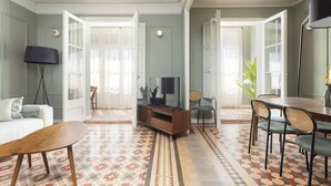 A spacious living area with a patterned floor, a sofa, a coffee table, a TV stand, and a dining area with chairs. - Spacious Stylish 4-BR Modernist Apartment (Barcelona)