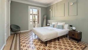 A bedroom with a large bed, a chair, a nightstand, and a view of the outside. - Spacious Stylish 4-BR Modernist Apartment (Barcelona)
