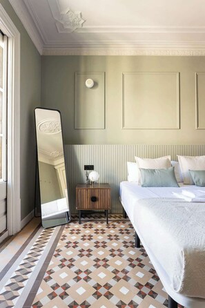 A hotel room with a large bed, a bedside table with a lamp, a mirror, and a patterned floor.