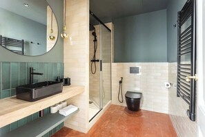 A modern bathroom with a glass-enclosed shower, a black sink, and a toilet.
