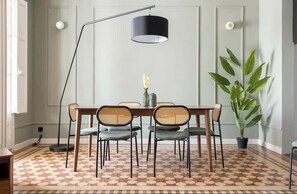 A dining area with a checkered floor, a wooden table, six chairs, a black pendant lamp, and a potted plant.