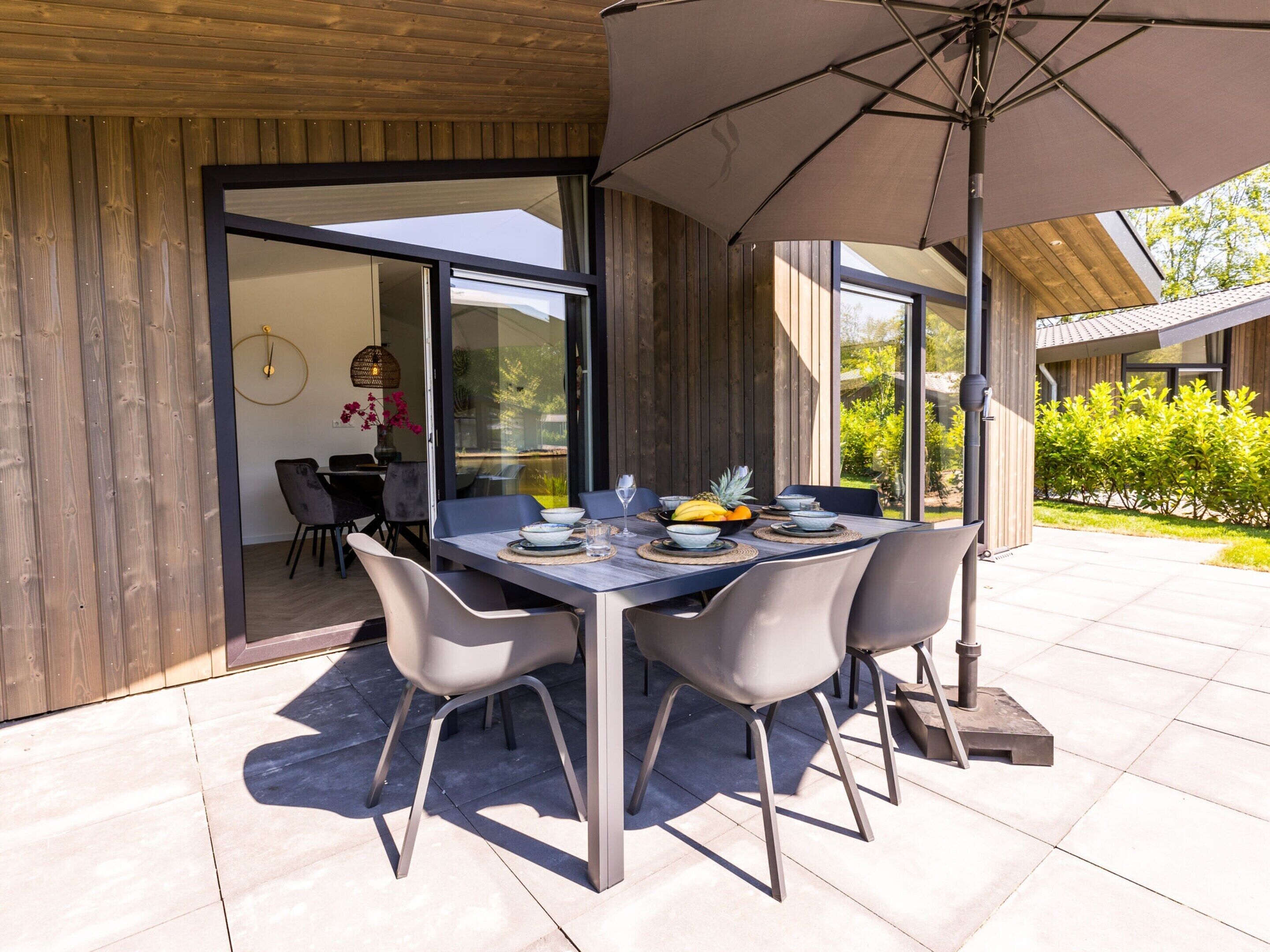An outdoor dining area with a table set for four, surrounded by chairs, under a large umbrella.