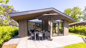 Un área de comedor exterior moderna con una mesa, sillas, un paraguas grande y un cerramiento de vidrio.