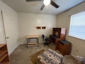 Un dormitorio con cama, escritorio, silla y ventilador de techo.