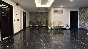 A modern lobby with a polished black marble floor, recessed ceiling lighting, and a stone wall with potted plants. - Hotel Creek Valley Mussoorie (Dehradun)