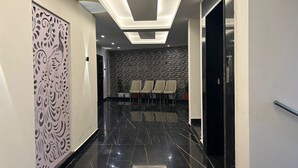 A modern hotel lobby with a black marble floor, a stone wall, and a decorative panel with a bird design. There are four chairs lined up against the wall. - Hotel Creek Valley Mussoorie (Dehradun)