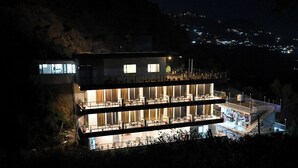 A multi-story building with balconies, large windows, and a well-lit interior. - Hotel Creek Valley Mussoorie (Dehradun)