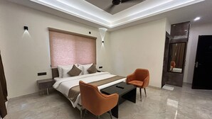 A modern bedroom with a bed, two chairs, a bedside table, a ceiling fan, and a door. - Hotel Creek Valley Mussoorie (Dehradun)