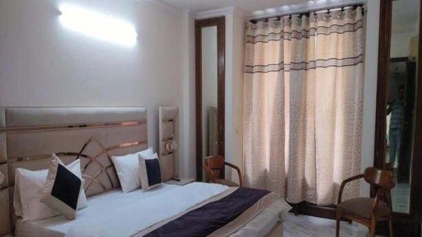 Quarto com cama, mesas de cabeceira, uma cadeira, um espelho e janela com cortinas.