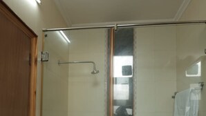 Casa de banho com cabine de duche em vidro, um balde branco e bancada de mármore.