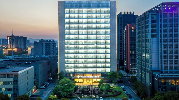 Un hotel moderno con un llamativo frente de vidrio, rodeado de otros edificios de gran altura.