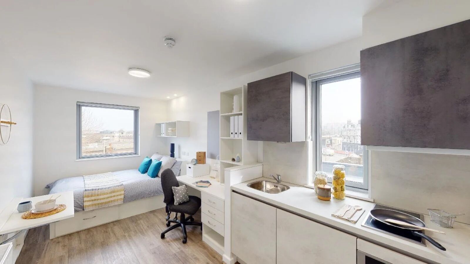 Ein kompaktes Studioapartment mit Bett, Küchenzeile und Blick auf die Stadt.