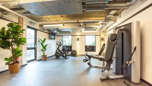 Ein Fitnessraum mit Trainingsgeräten, einer großen Topfpflanze und Blick ins Freie.