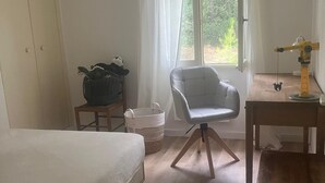 Un dormitorio con cama, una silla, un escritorio y una ventana con cortinas.