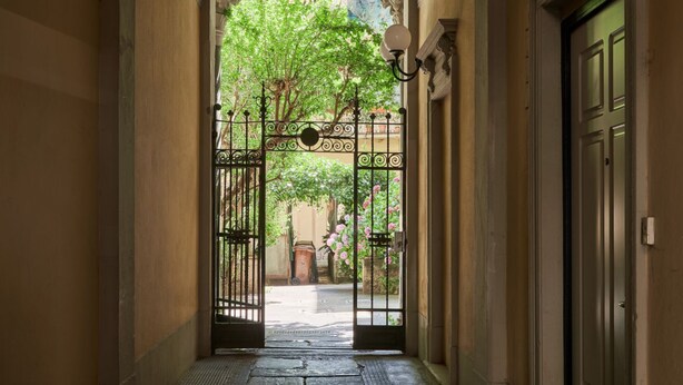 A hallway with a wrought iron gate leading to a courtyard with trees and flowers.