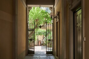 Un couloir avec une grille en fer forgé donnant sur une cour intérieure agrémentée d’arbres et de fleurs.
