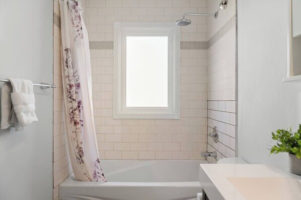 A modern bathroom with a shower, a window, and a sink.