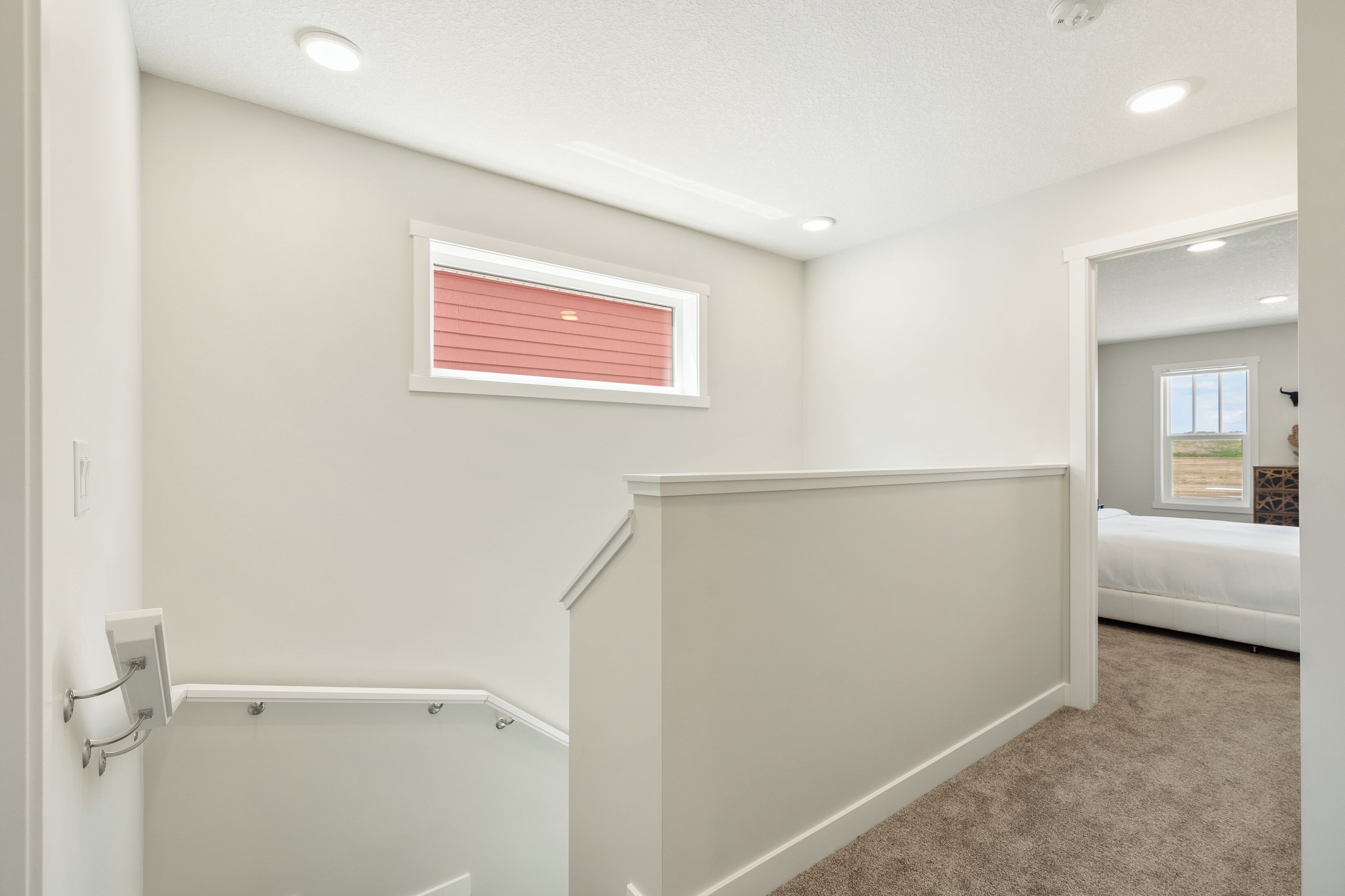 A hallway with a carpeted floor, a window with blinds, and a door with a light switch.