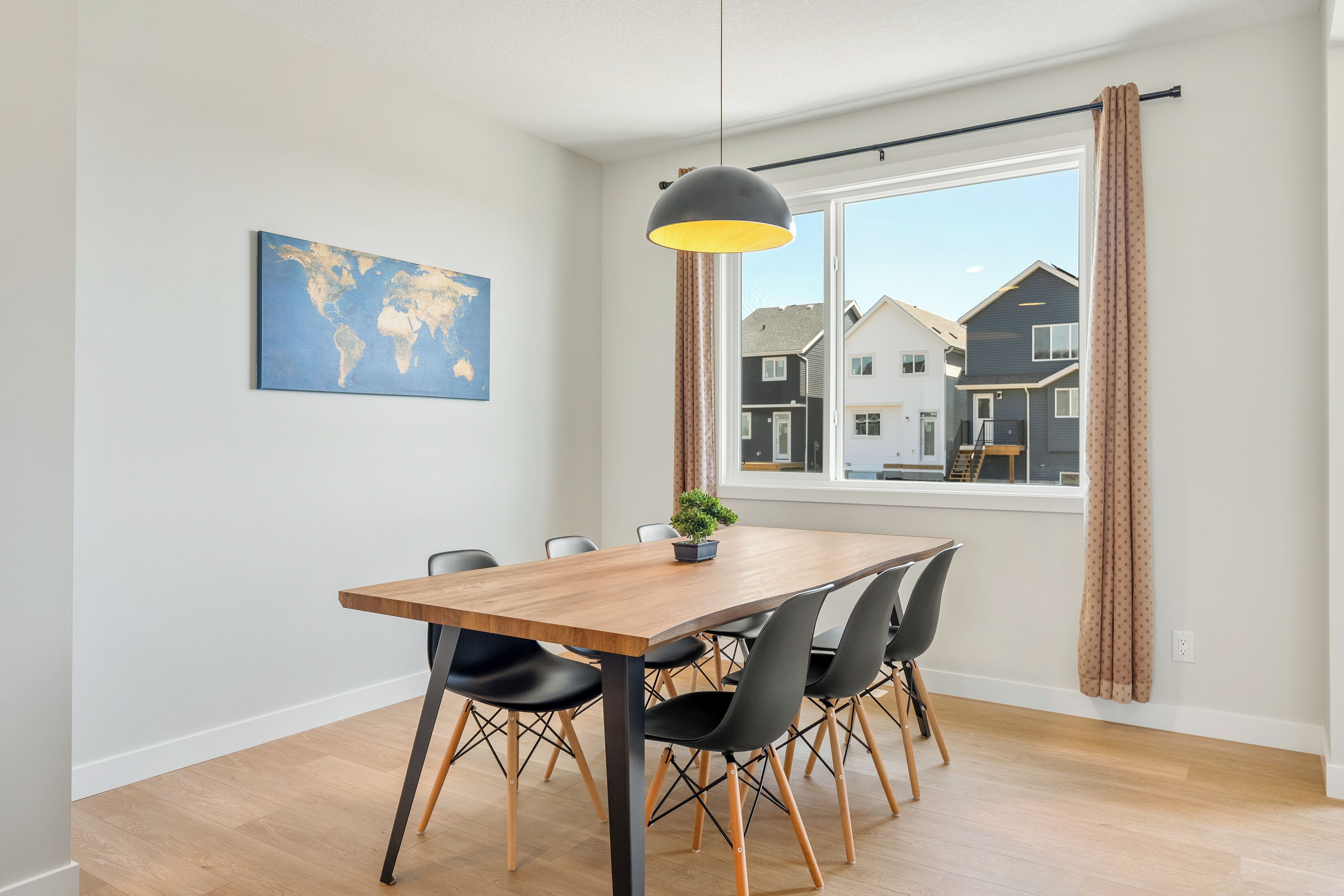A dining area with a wooden table, black chairs, a hanging pendant light, a small potted plant, and a world map on the wall.