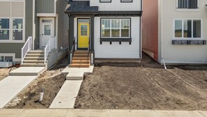 Ett modernt hus i två våningar med en gul ytterdörr, en liten veranda och en synlig trappa som leder upp till entrén.