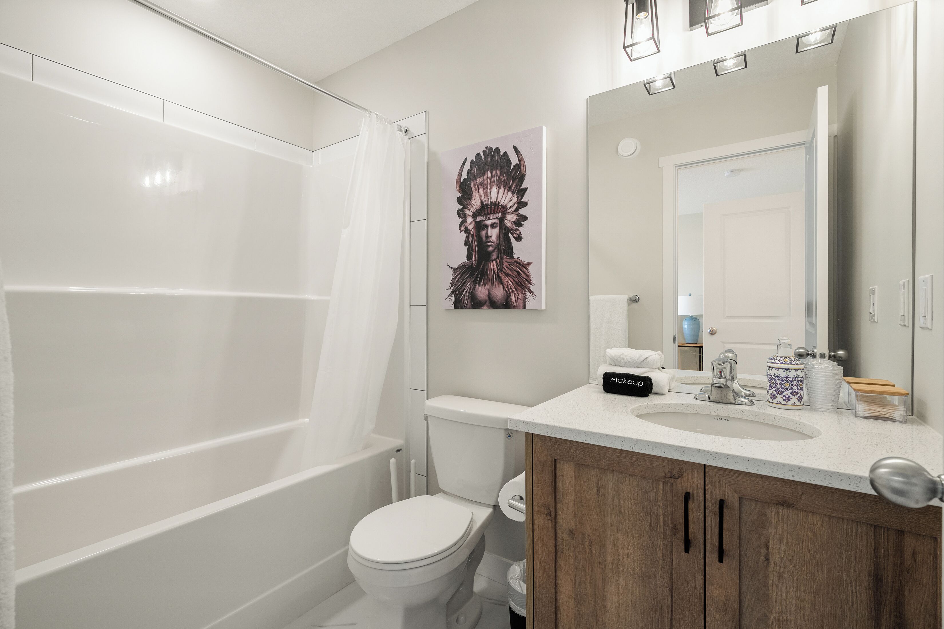A modern bathroom with a white toilet, a shower, a sink with a mirror, and a decorative painting on the wall.