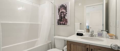 A modern bathroom with a white toilet, a shower, a sink with a mirror, and a decorative painting on the wall.