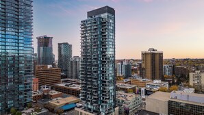 Um edifício alto com várias varandas, rodeado por outros edifícios e um céu limpo.