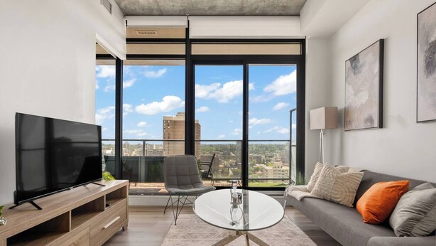 Uma sala de estar moderna com uma televisão grande, um sofá, uma mesa de centro e uma poltrona.
