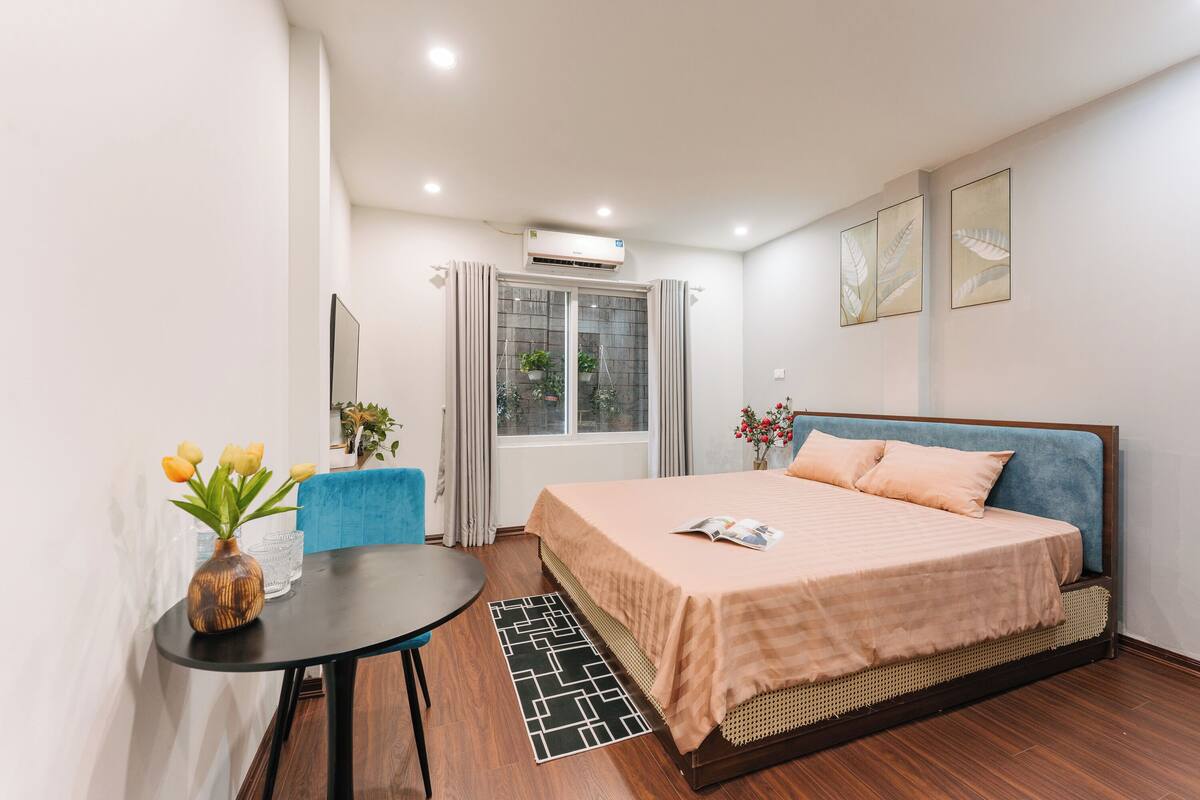 A bedroom with a bed, a small table with a vase, and a window with curtains.