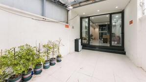 Un espacio interior limpio y con baldosas, con plantas en macetas y una puerta de vidrio que da a una habitación.
