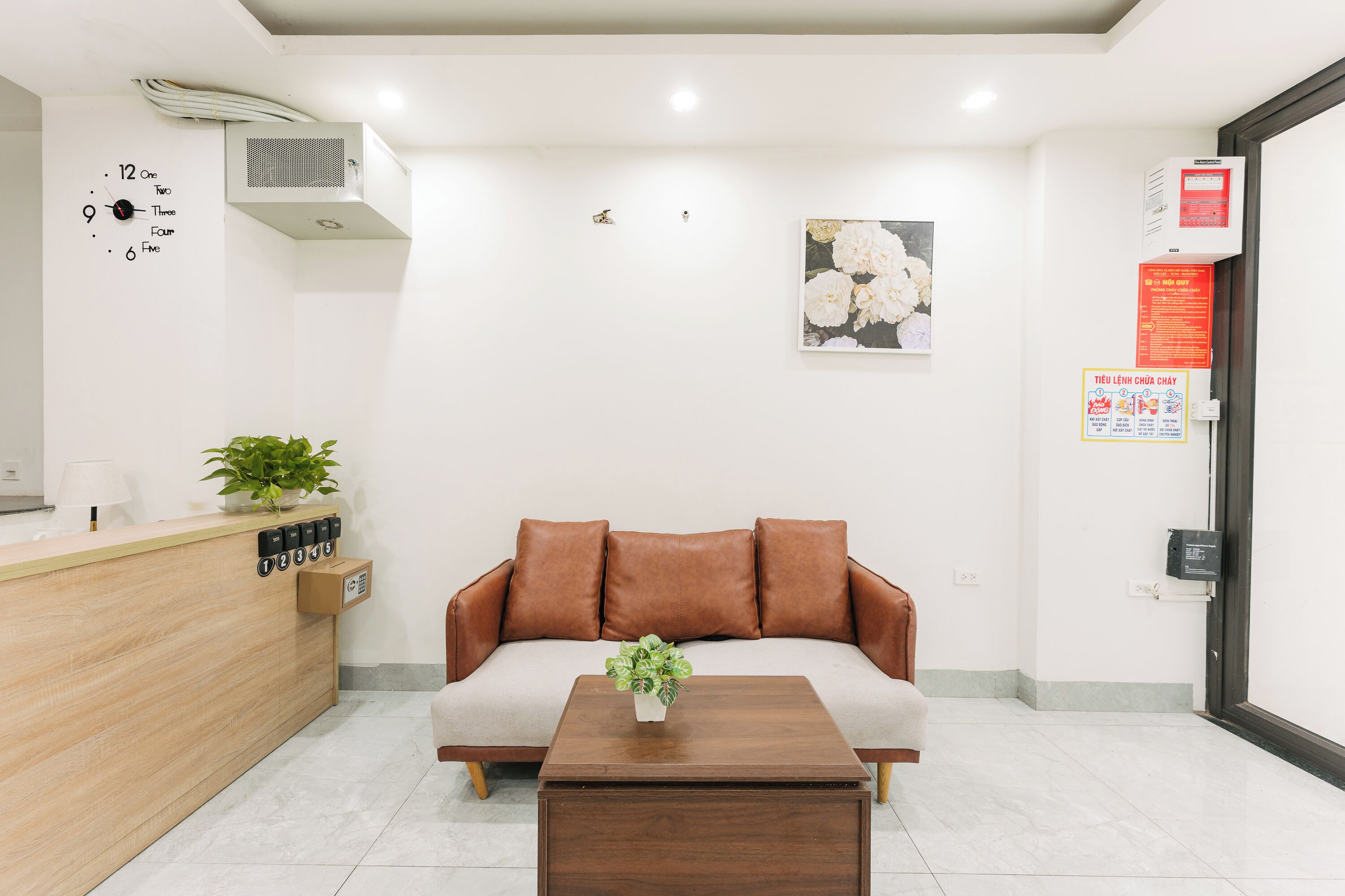 A reception area with a wooden counter, a brown sofa, a coffee table, and a wall clock.