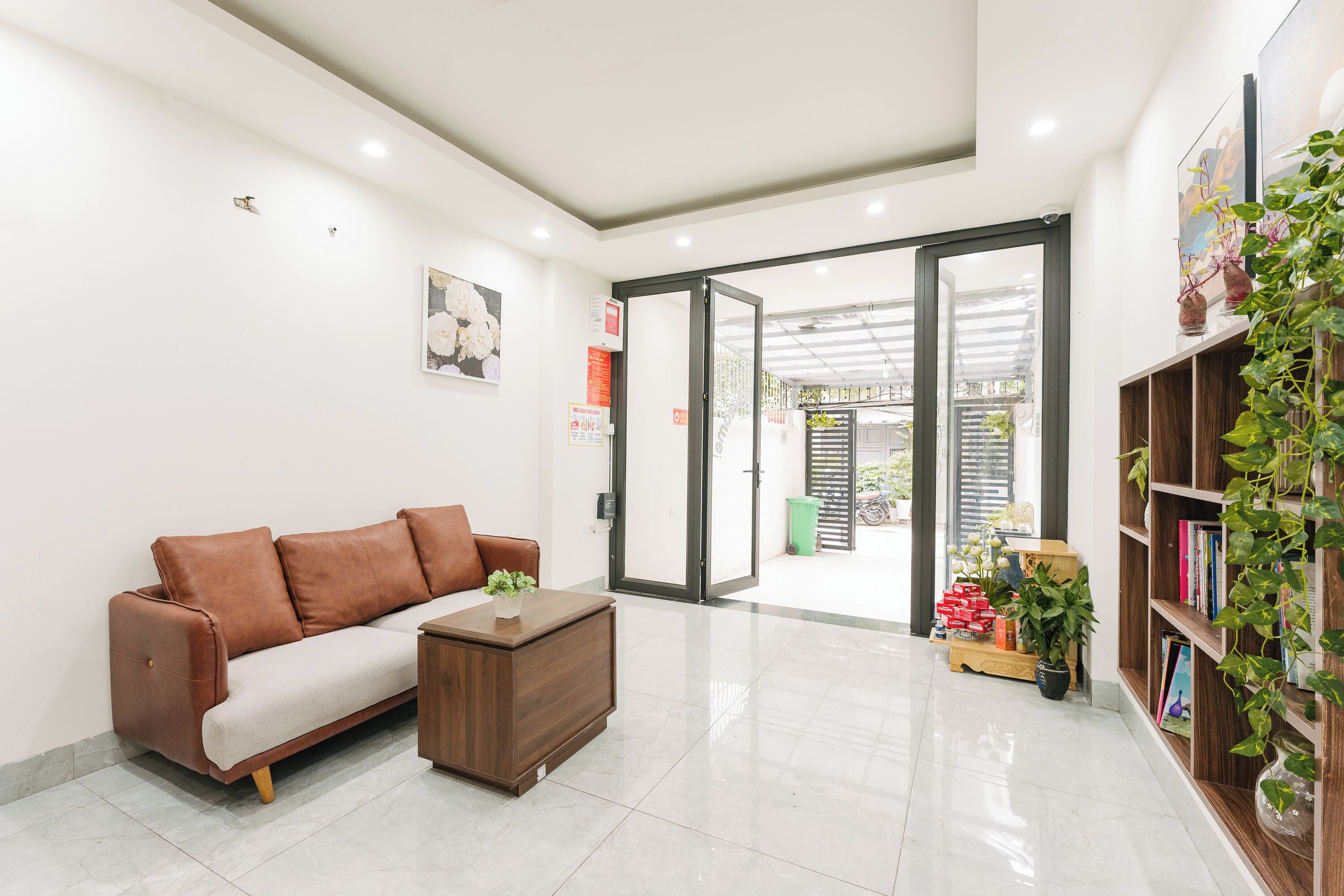 A modern living room with a brown leather sofa, a wooden coffee table, and a bookshelf with plants.