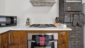 Une cuisine moderne équipée d’un four à micro-ondes encastré, d’une cuisinière à gaz, d’un four et d’une hotte en acier inoxydable. On y trouve des armoires en bois, un bloc à couteaux et des maniques suspendues.