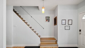Un escalier avec des marches en bois et un mur blanc. Un tapis noir se trouve au pied de l’escalier.