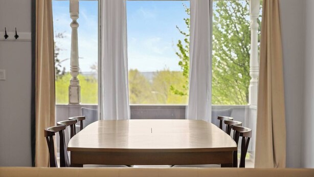Une table à manger avec des chaises, dans une pièce dotée de grandes fenêtres et de rideaux blancs.