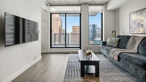 Un salon moderne avec un grand téléviseur à écran plat, un canapé gris foncé et un tapis à motifs.