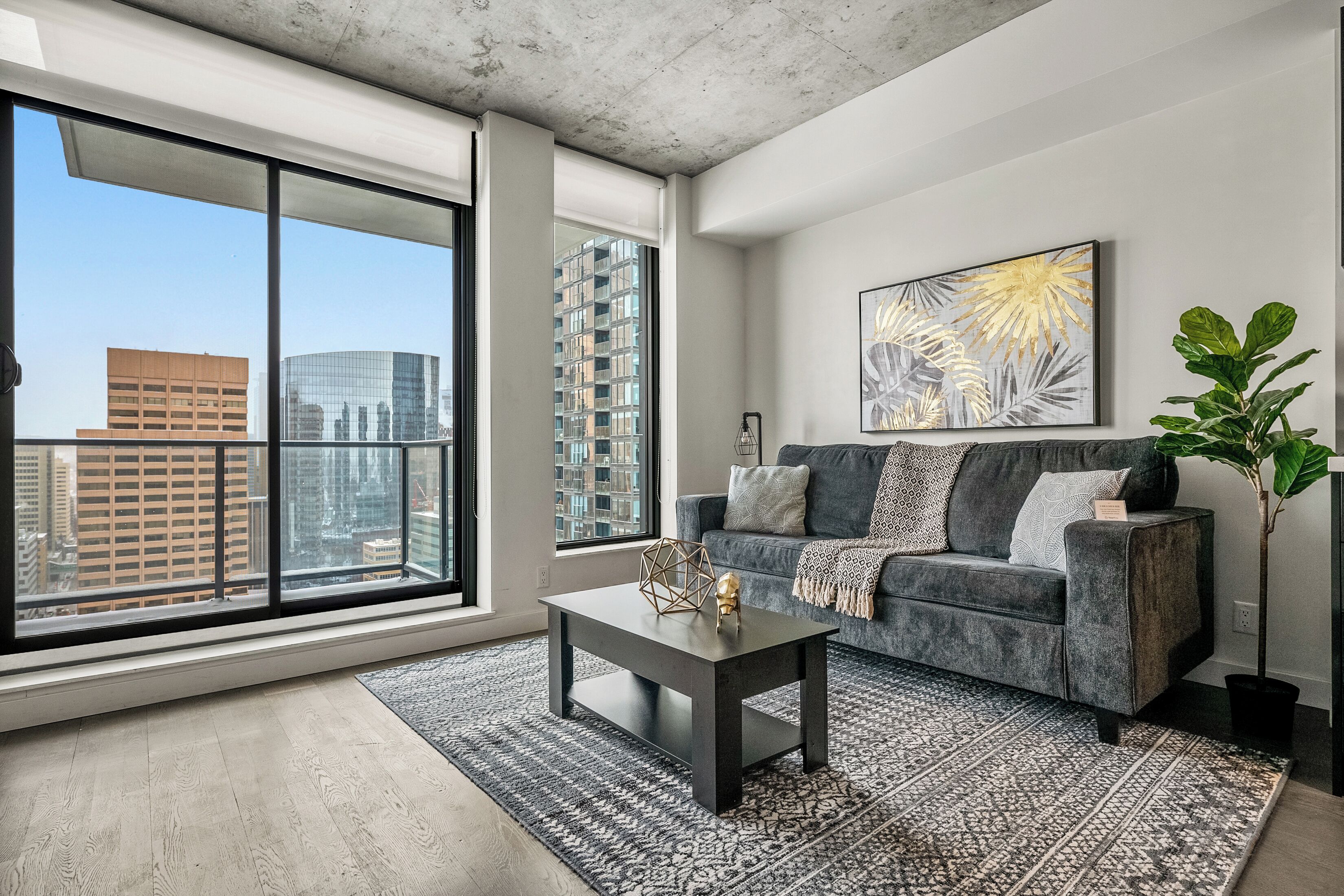 A modern living room with a large window, a gray sofa, a patterned rug, and a city view.