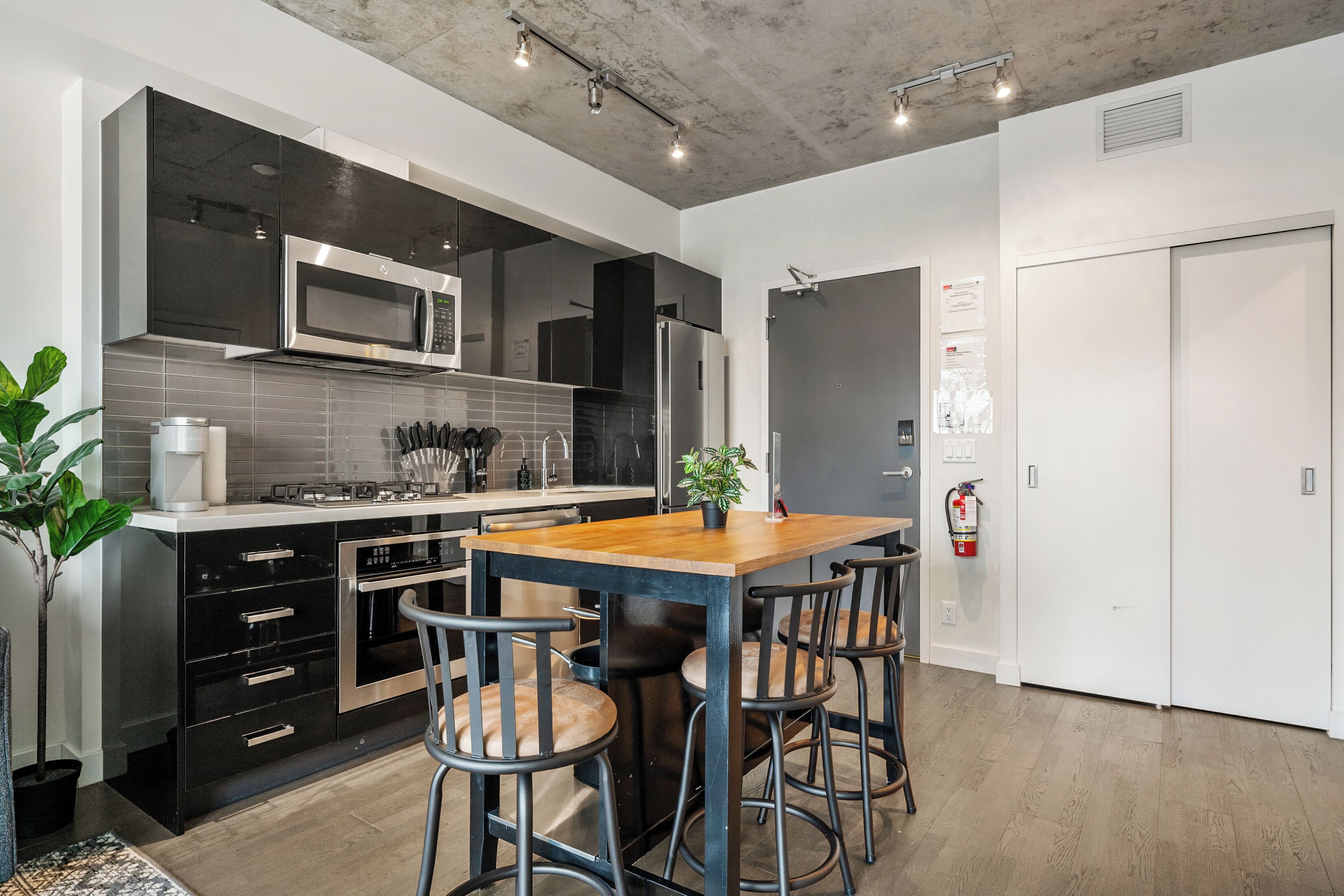 Une cuisine moderne avec des meubles de rangement noirs, un four à micro-ondes en acier inoxydable et un îlot central en bois doté de tabourets de bar.