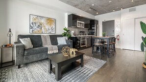 Un salon moderne avec un canapé gris, une table basse et une cuisine en arrière-plan.